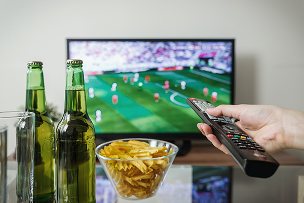 Person watching football on TV having snacks and drinks