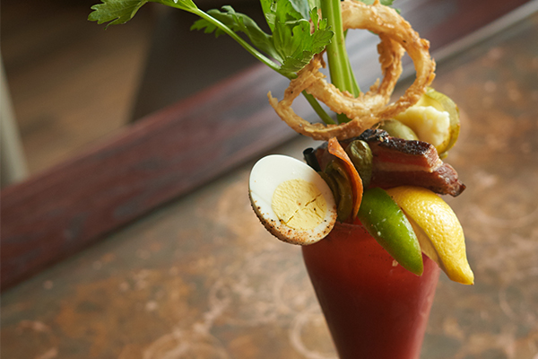 Bloody Mary with onion ring, celery, lemon, lime, bacon and boiled egg garnish.